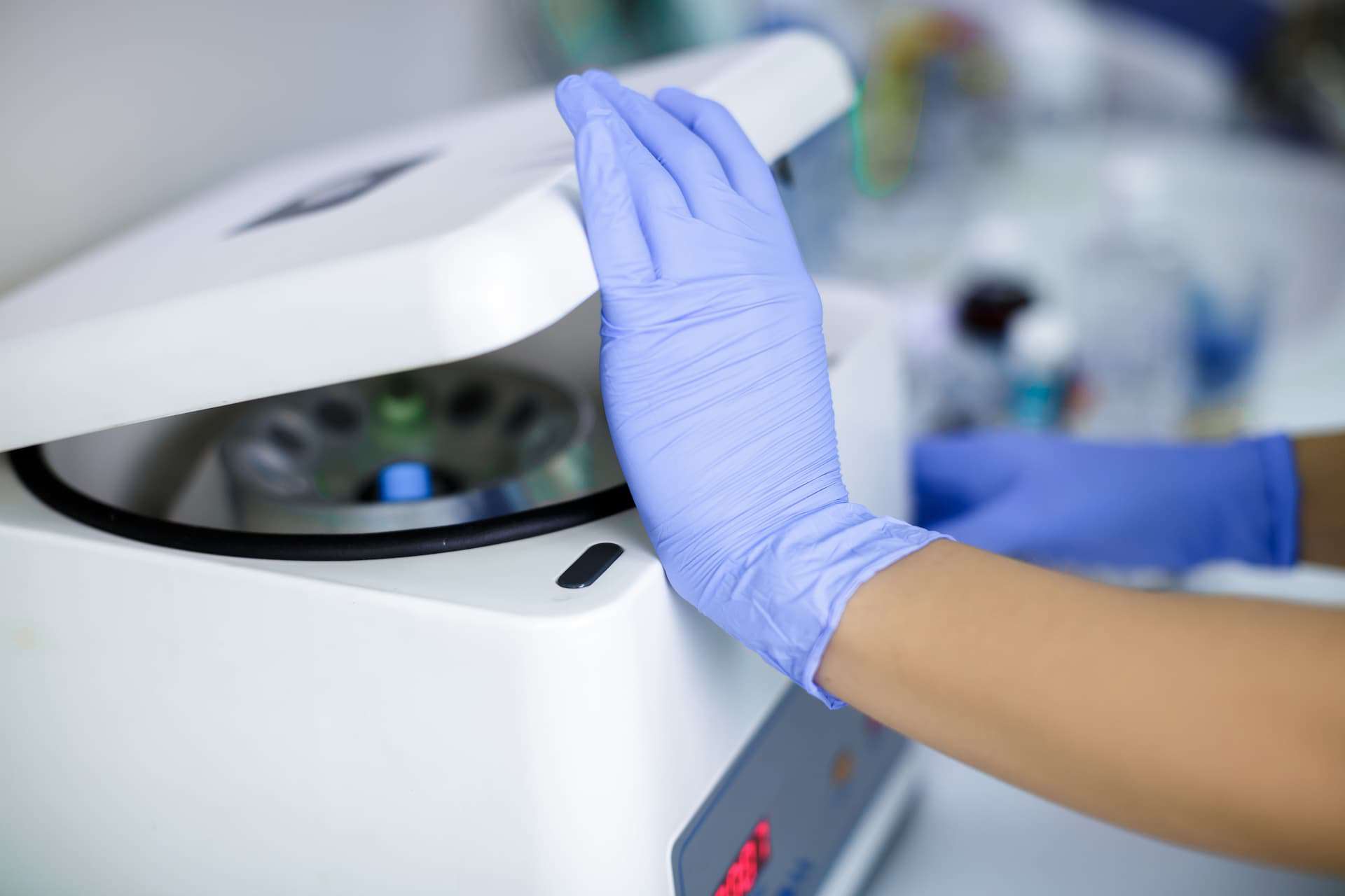 A person wearing gloves is closing the lid on a centrifuge.