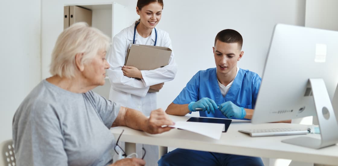 A doctor is leaning over the shoulder of a lab technician while talking to a patient.